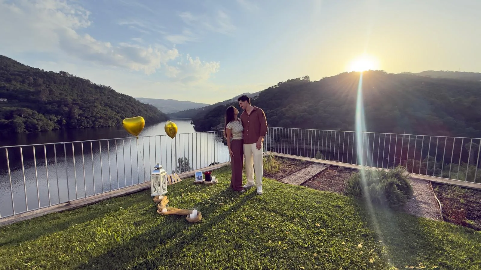 A Ana e o Daniel no terraço sobre o rio Douro ao pôr do sol, com balões dourados em forma de coração
